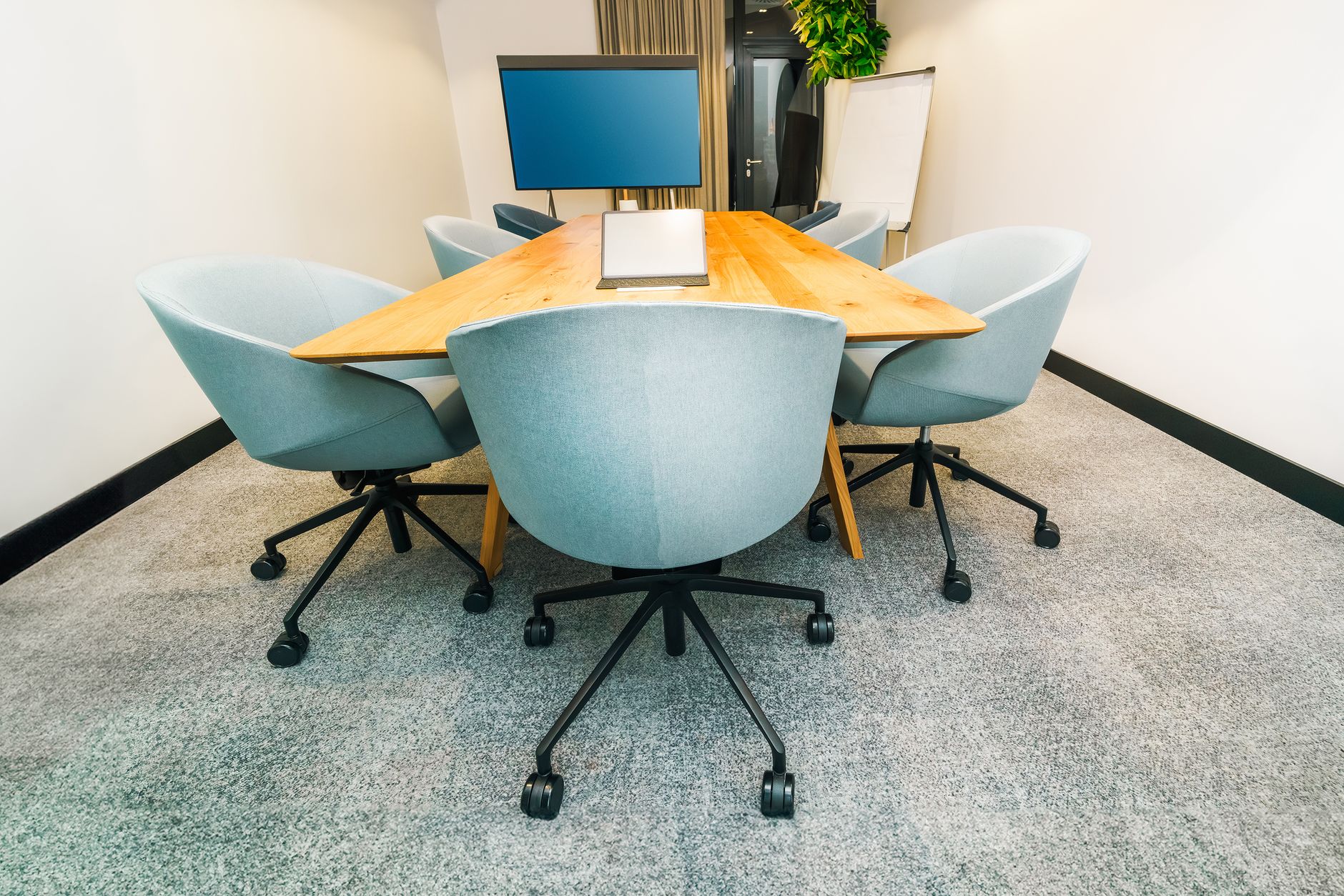 A laptop open on a meeting room table with notebooks and coffee cups around it