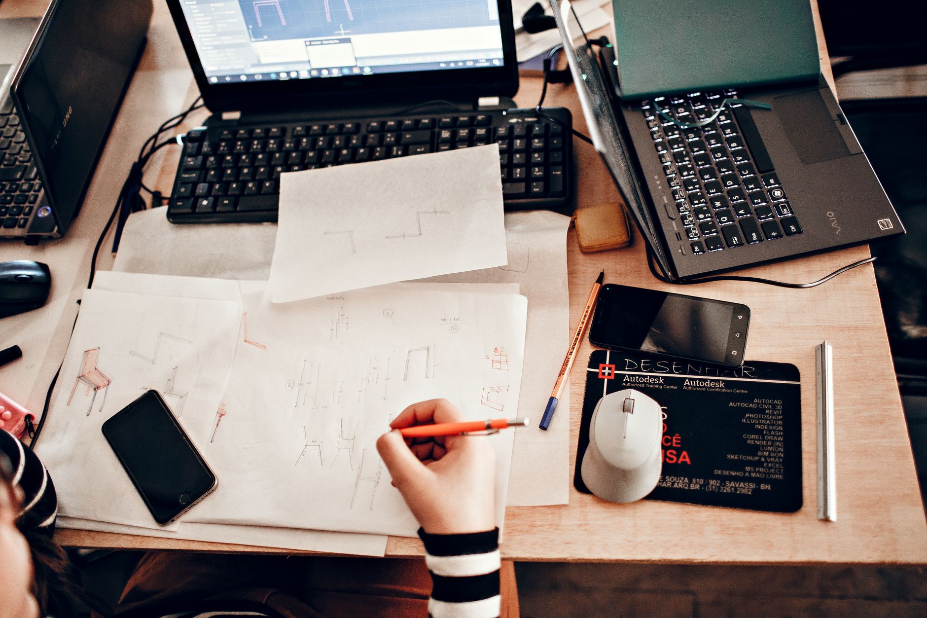 A laptop on a studio desk beside pencil sketches of logo ideas and colour swatches