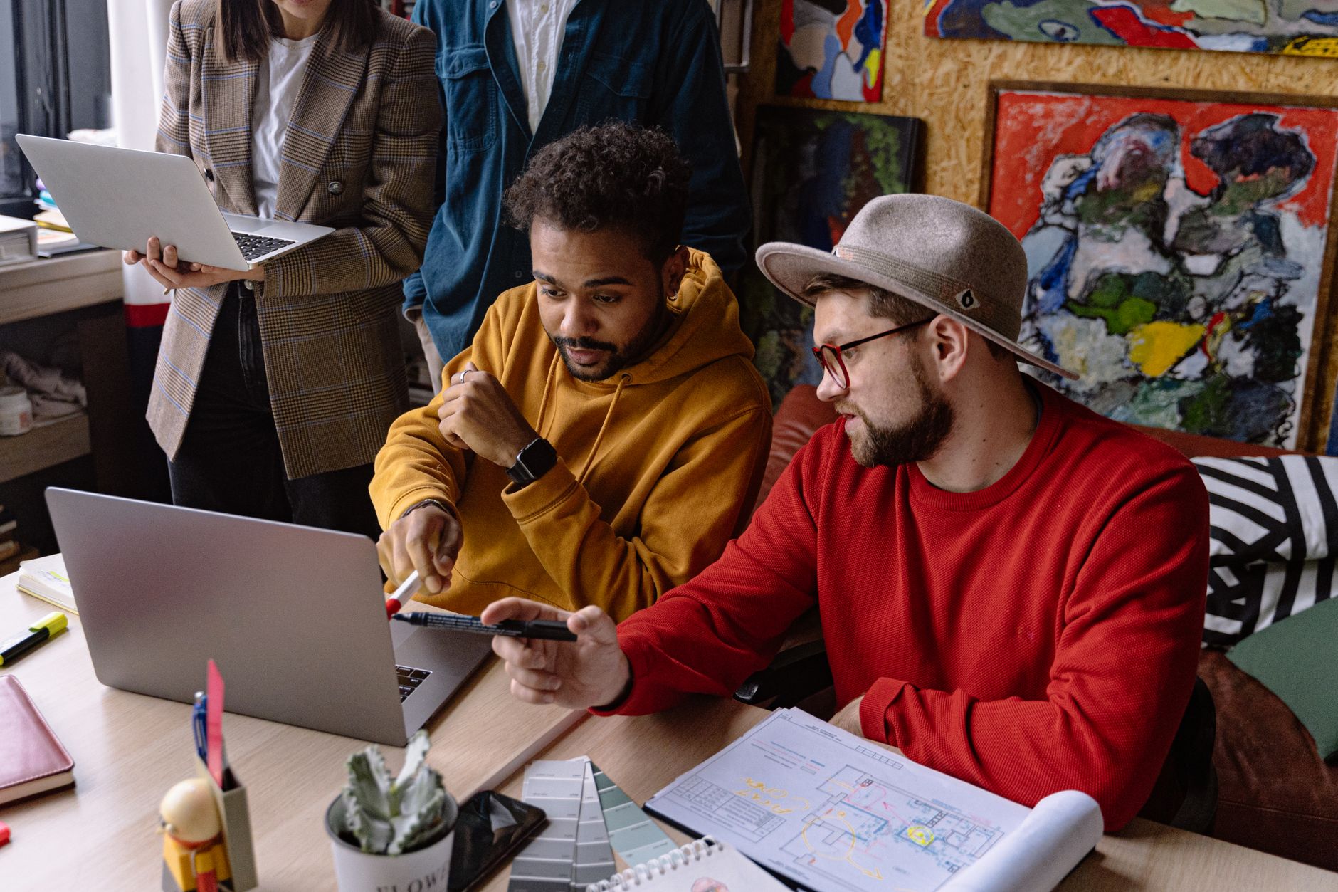 Designers at a studio table looking at a project plan on a laptop next to printed brand sketches