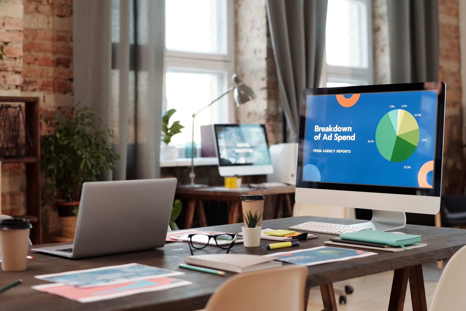 A laptop on a studio desk showing a branded proposal layout next to printed packaging samples