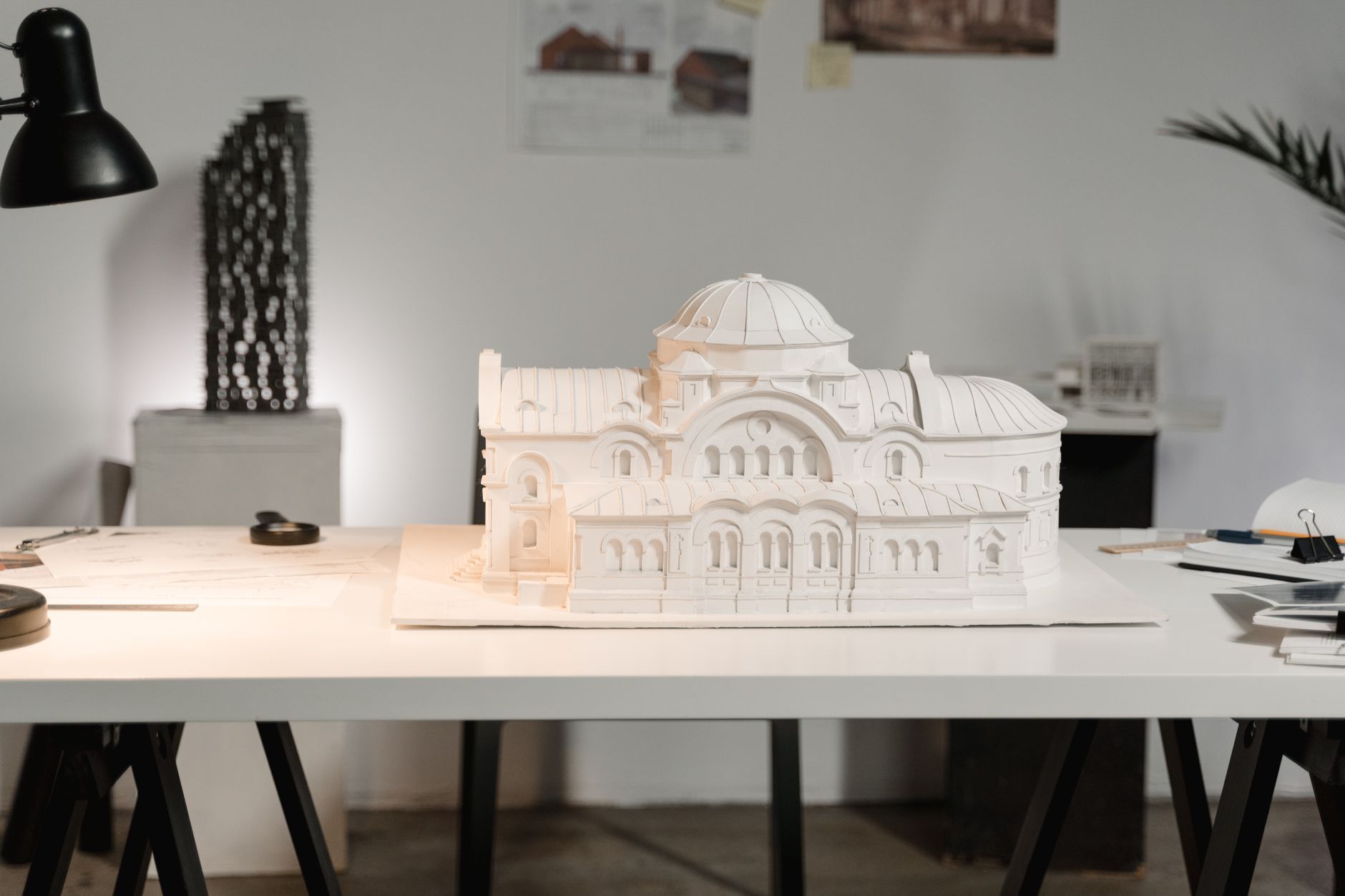 A white architectural model on a studio table next to drawings