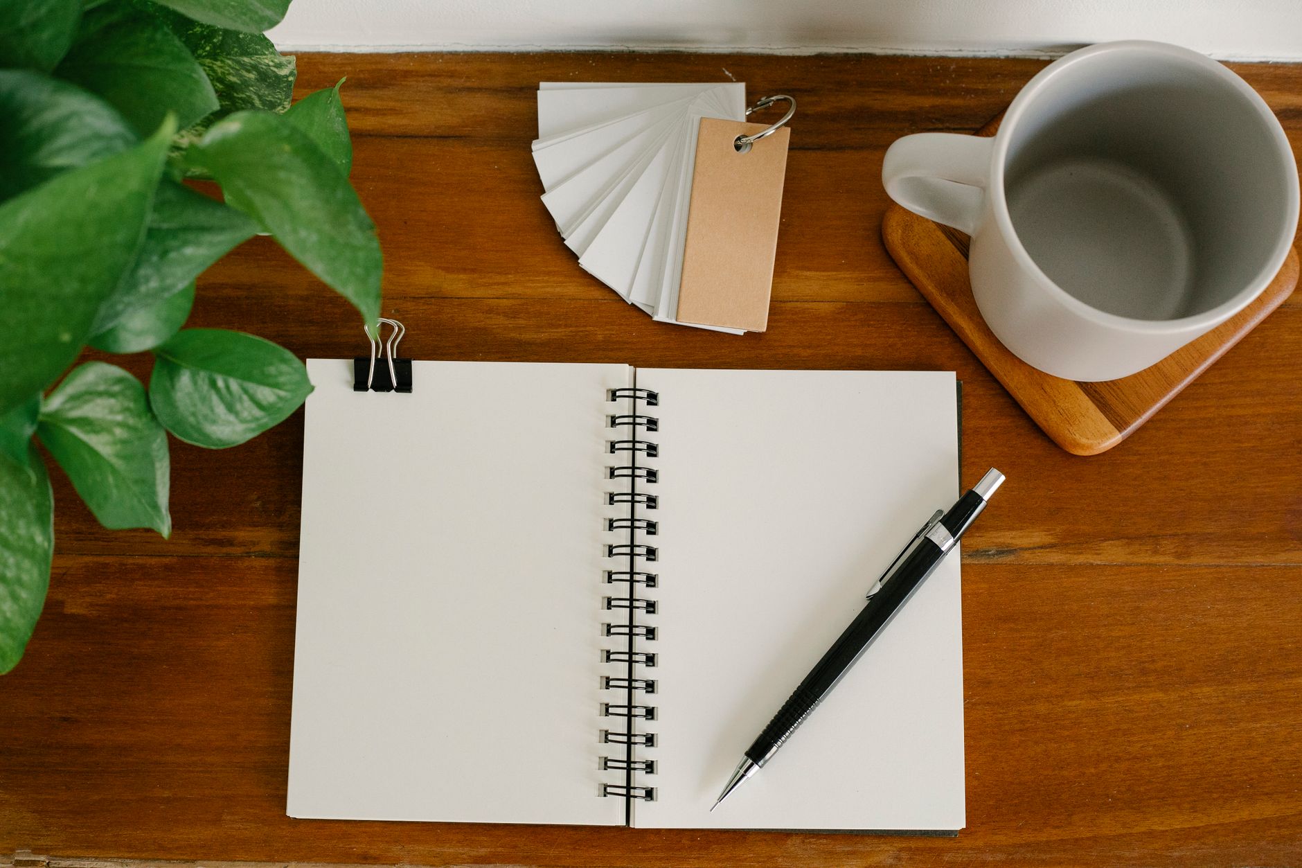 An open notebook, a pen and a coffee cup on a wooden desk