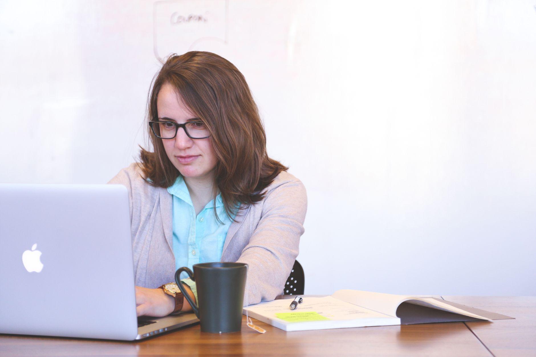 A laptop open on a studio desk beside printed brand sketches and a notebook